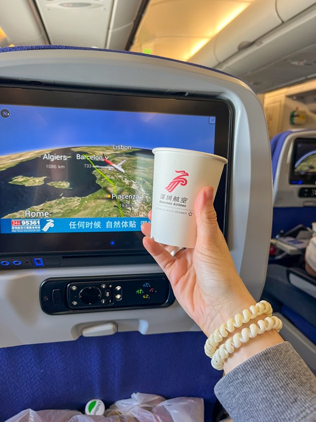 Pantalla del asiento mostrando el mapa de vuelo desde Barcelona junto a un vaso de Shenzhen Airlines